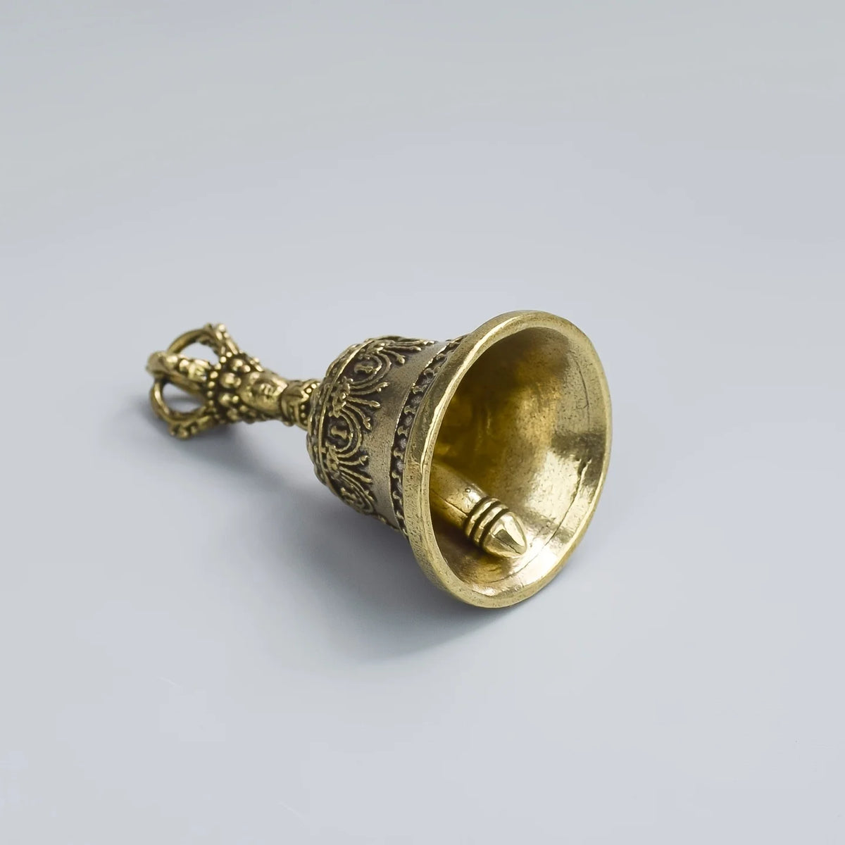 Sifflet de cloche en bronze avec un dessus orné et une coupe évasée, sur fond gris clair.