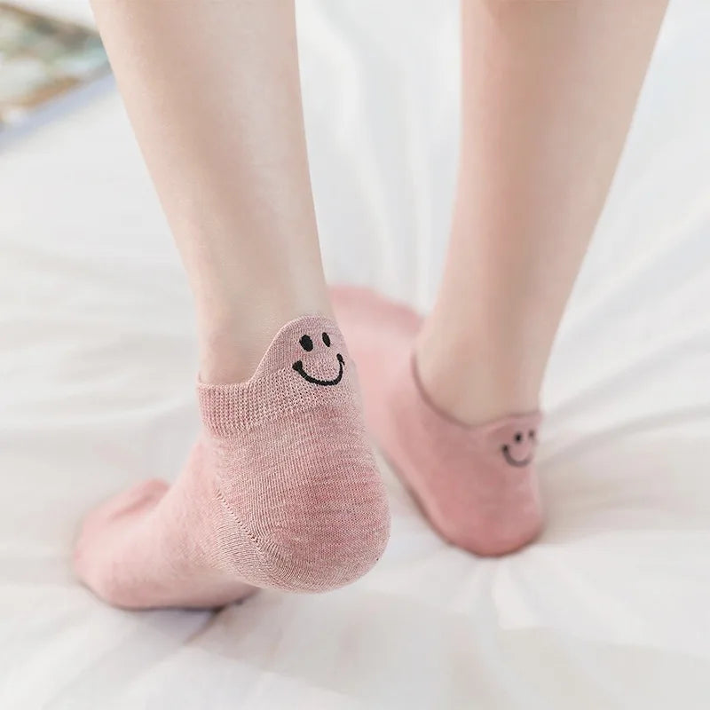 Un par de calcetines de punto rosas con caras sonrientes bordadas, sobre una superficie blanca.