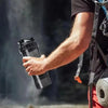 A person holds a black leak-proof protein shaker bottle with a pill tray in their hand.