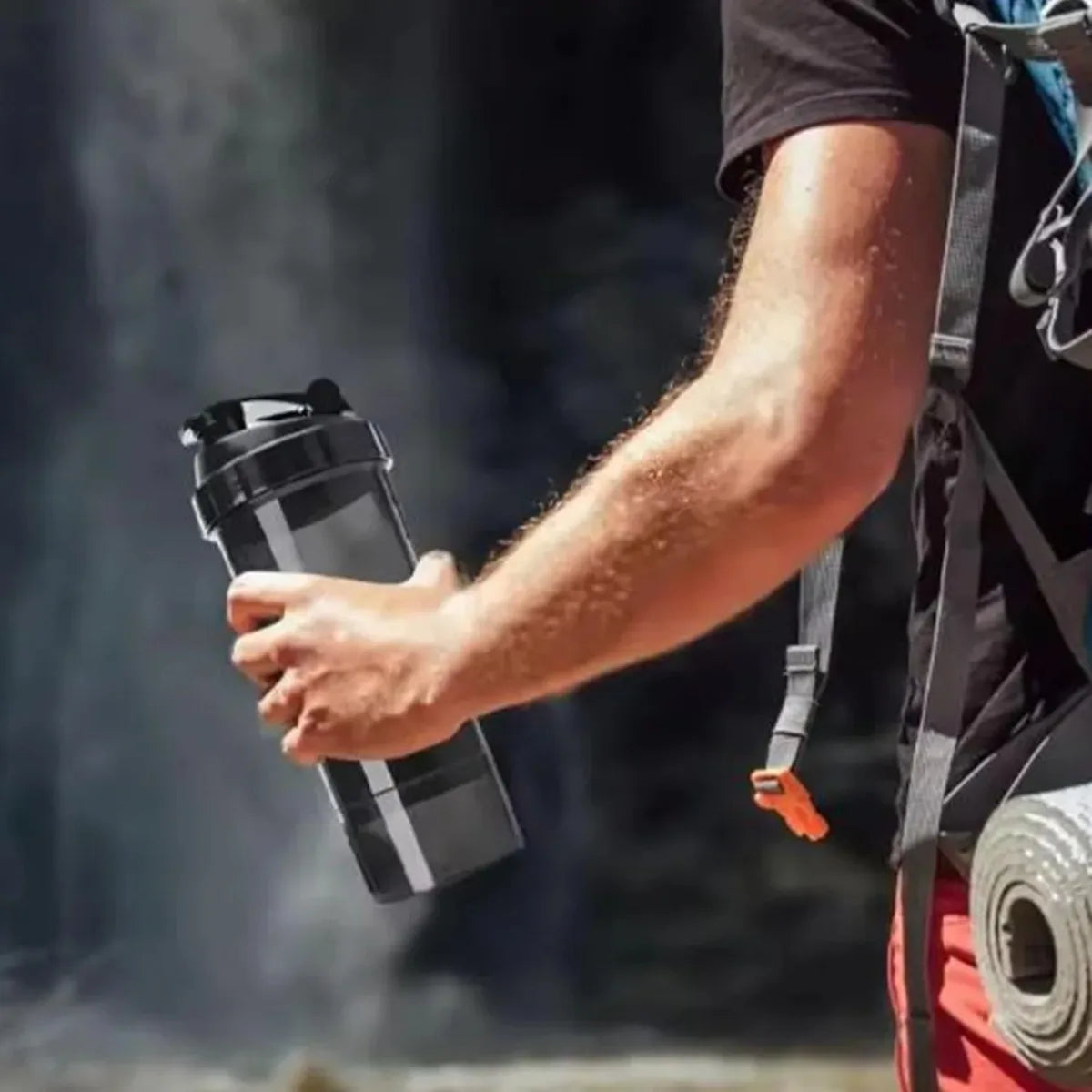 A person holds a black leak-proof protein shaker bottle with a pill tray in their hand.