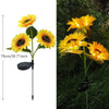 A bright yellow sunflower with a dark center is illuminated by an LED light on a stake.