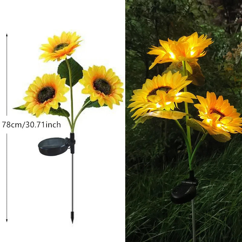A bright yellow sunflower with a dark center is illuminated by an LED light on a stake.