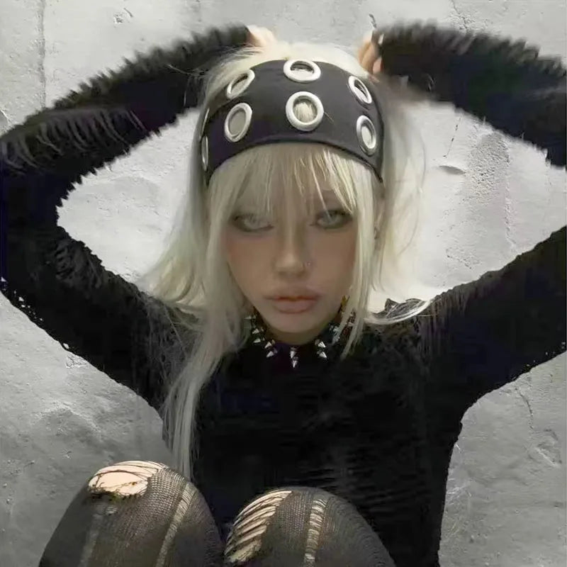 Une femme aux longs cheveux blancs portant un bandeau à œillets noir et un haut noir contre un mur gris.