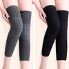 A pair of thick wool knee warmers in charcoal gray and black, shown on a model's legs.