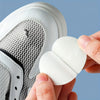 A hand is applying a white self-adhesive shoe repair patch onto the sole of a white athletic shoe.
