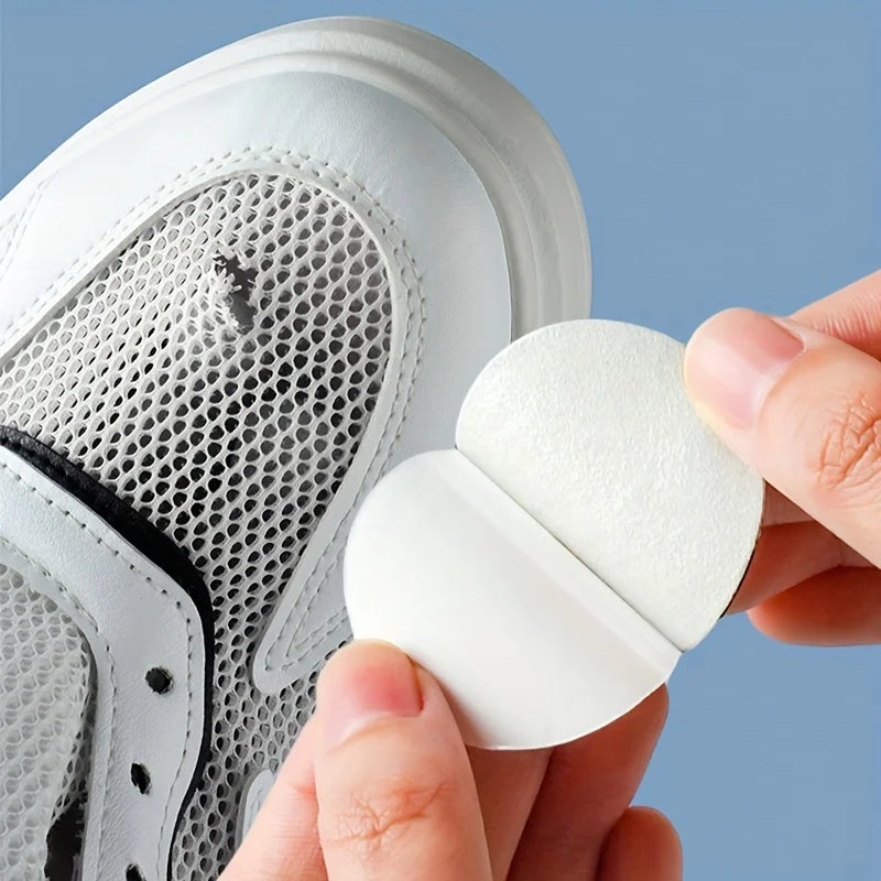 A hand is applying a white self-adhesive shoe repair patch onto the sole of a white athletic shoe.
