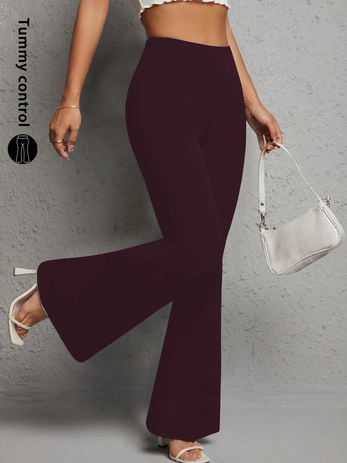 A model wearing dark plum flared yoga trousers and a white shoulder bag.