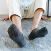 A close-up shot of a person's feet wearing dark gray invisible silicone no-show socks on a light gray floor.
