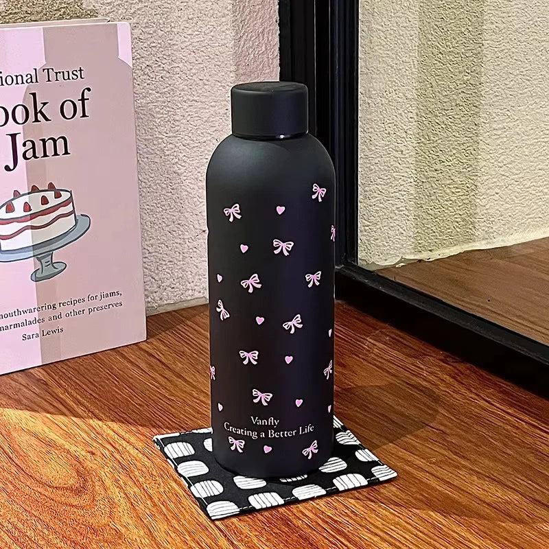 Taza de viaje de acero inoxidable aislada de doble pared color negro con diseños de mariposa rosa sobre una superficie de mad