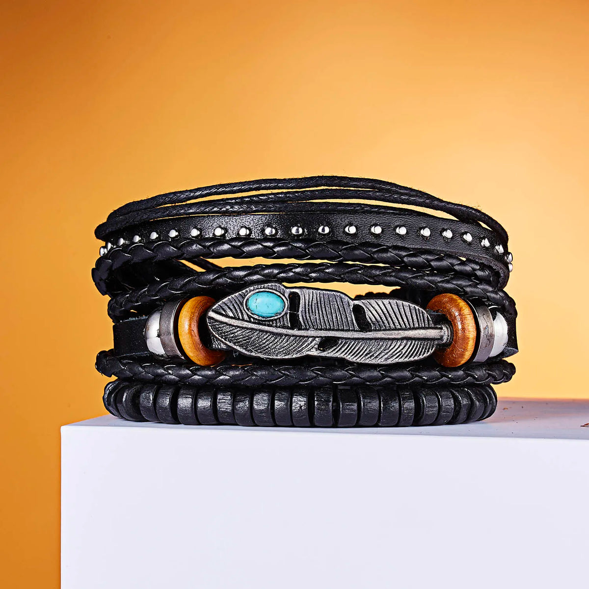 Stapel schwarzer Lederarmbänder mit silbernen Blattfeder- und kleinen Stecker-Charms auf orangem Hintergrund