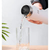 A hand pours water from an insulated stainless steel thermal water bottle into a glass.