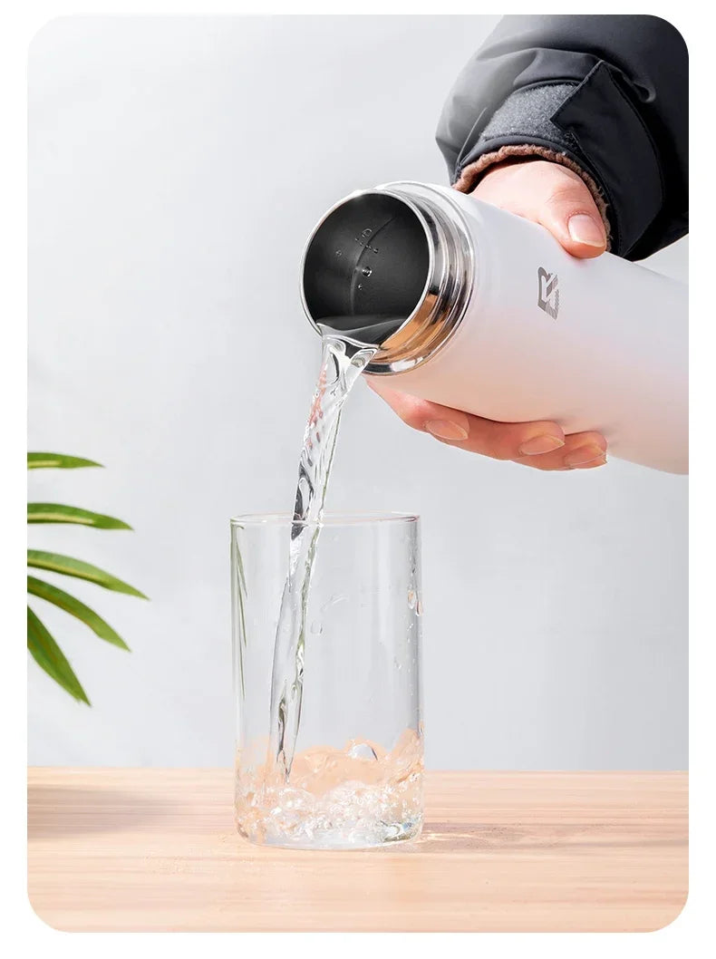 A hand pours water from an insulated stainless steel thermal water bottle into a glass.