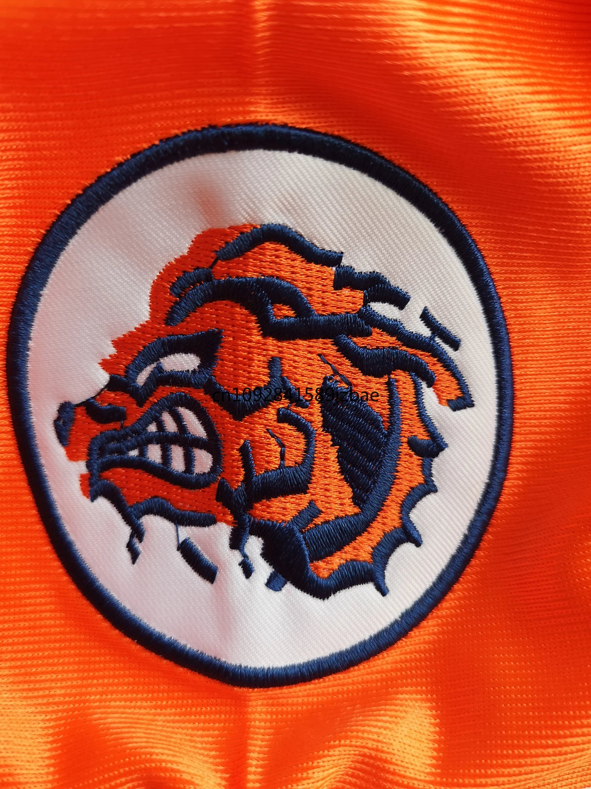 Rundes besticktes Patch mit stilisiertem braun-weißen Bärenkopf in orange und marineblau auf weißem Hintergrund, vor orangefa
