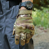 Une main portant des gants tactiques camouflage, avec une montre noire, tenue contre un vêtement sombre.