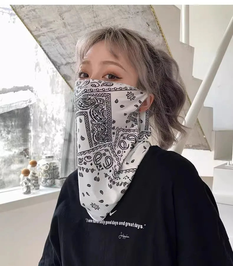 Una persona vistiendo una camisa negra de manga larga y una bufanda protectora UV con estampado paisley blanca cubriendo su c