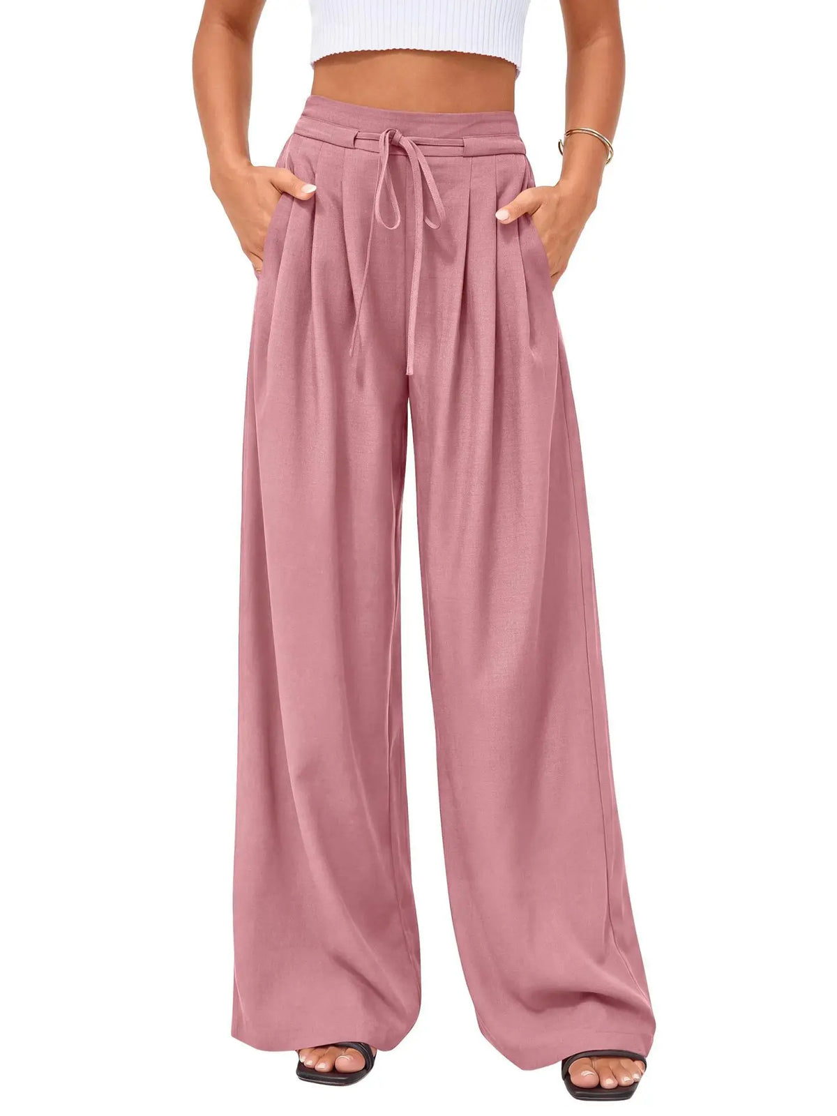 A model is wearing dusty rose flowy high waist drawstring wide leg pants with a white cropped top.