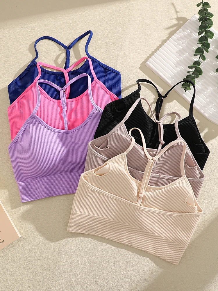 A collection of ribbed crop tops and sports bras in various shades of pink, purple, blue, and black laid out on a light surfa