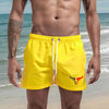 A muscular man wearing bright yellow quick-drying swim shorts on a beach.