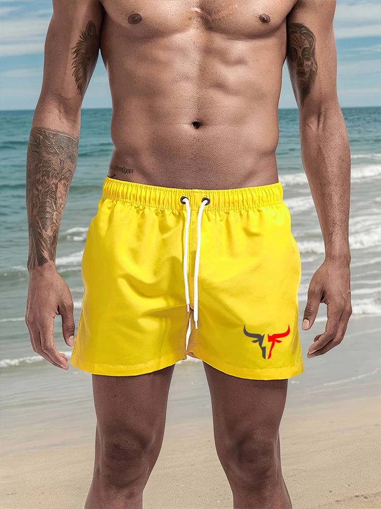 A muscular man wearing bright yellow quick-drying swim shorts on a beach.