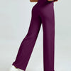 A woman is modeling high waisted purple yoga pants with a white top and white sneakers.