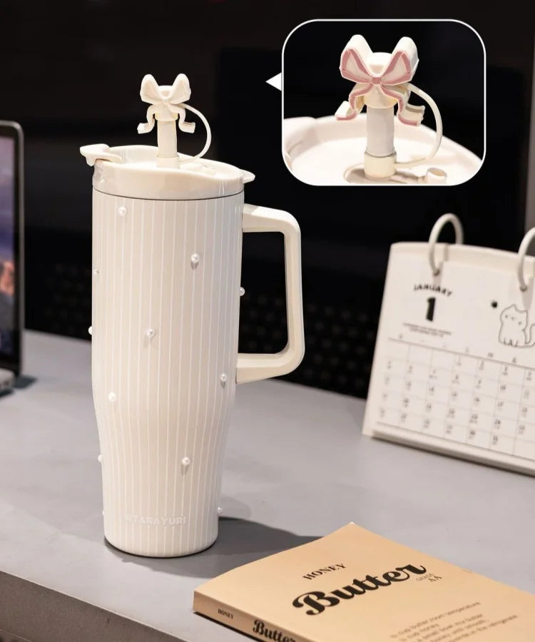 A white insulated thermos mug with a lid and handle is shown next to a calendar and a book.