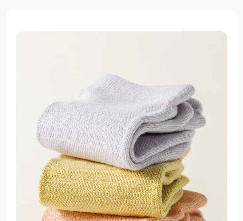 Une pile de chaussettes de yoga et de sport en tricot doux dans les tons violet clair, jaune pâle et pêche.