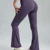 A model wearing high-waisted bootcut yoga pants in purple and white sneakers.