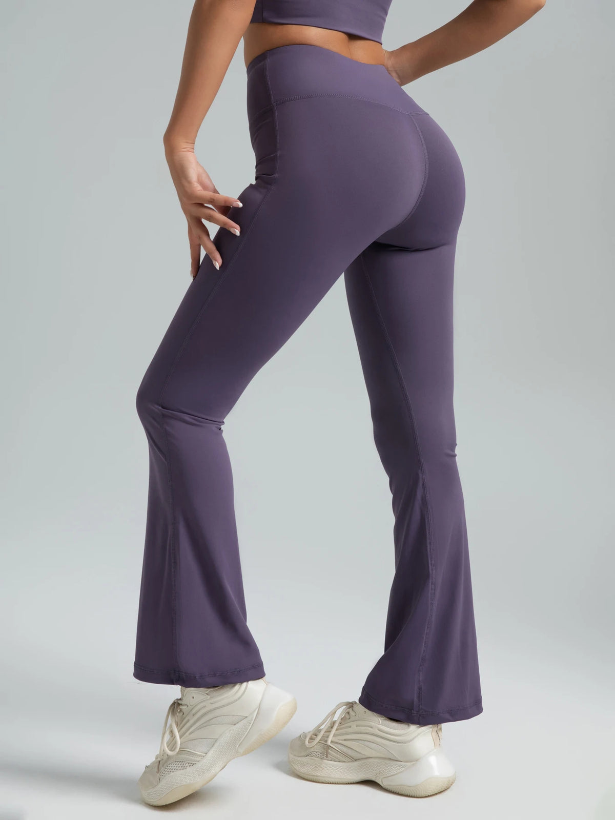 A model wearing high-waisted bootcut yoga pants in purple and white sneakers.
