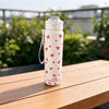A white tumbler with a floral pattern sits on a wooden table outdoors.