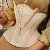 A close-up of a beige double compression waist trainer corset body shaper worn under a gold textured top.