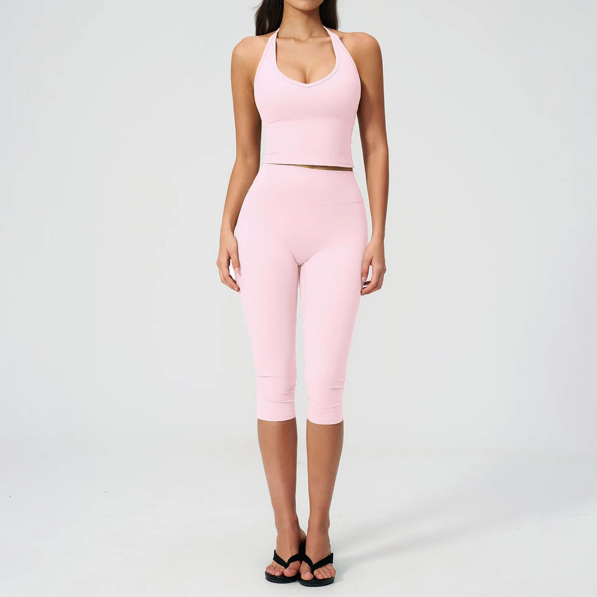 A woman wearing a pink women's premium fitness tracksuit consisting of a cropped tank top and matching leggings.