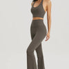 A woman wearing a taupe halter neck sports bra top and matching leggings posing against a light gray background.