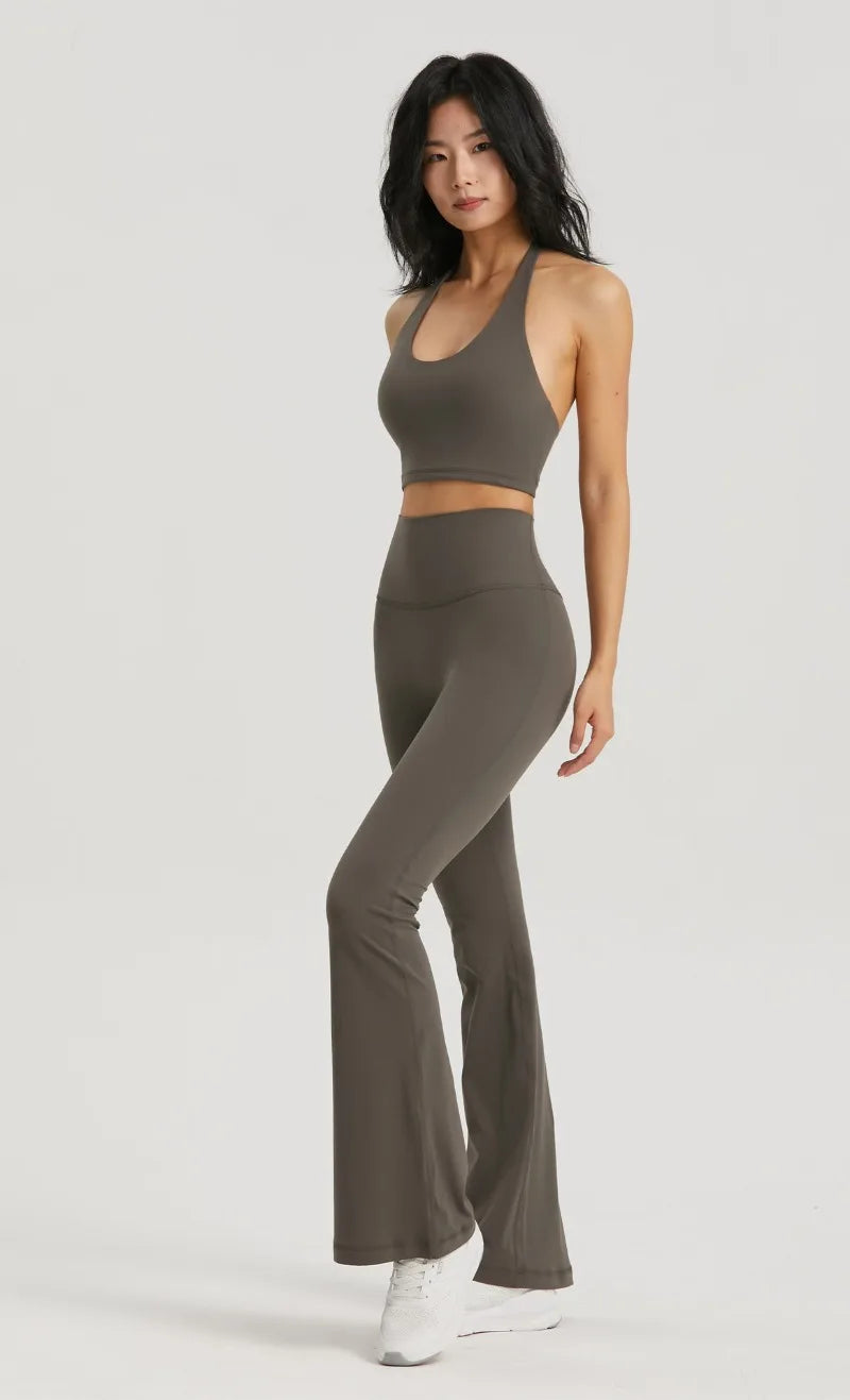A woman wearing a taupe halter neck sports bra top and matching leggings posing against a light gray background.