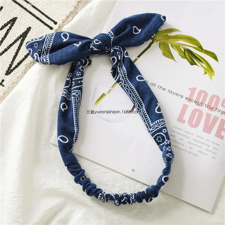 Un bandeau bohème à motif paisley bleu marine noué en nœud, posé sur une surface blanche à côté d'un livre.