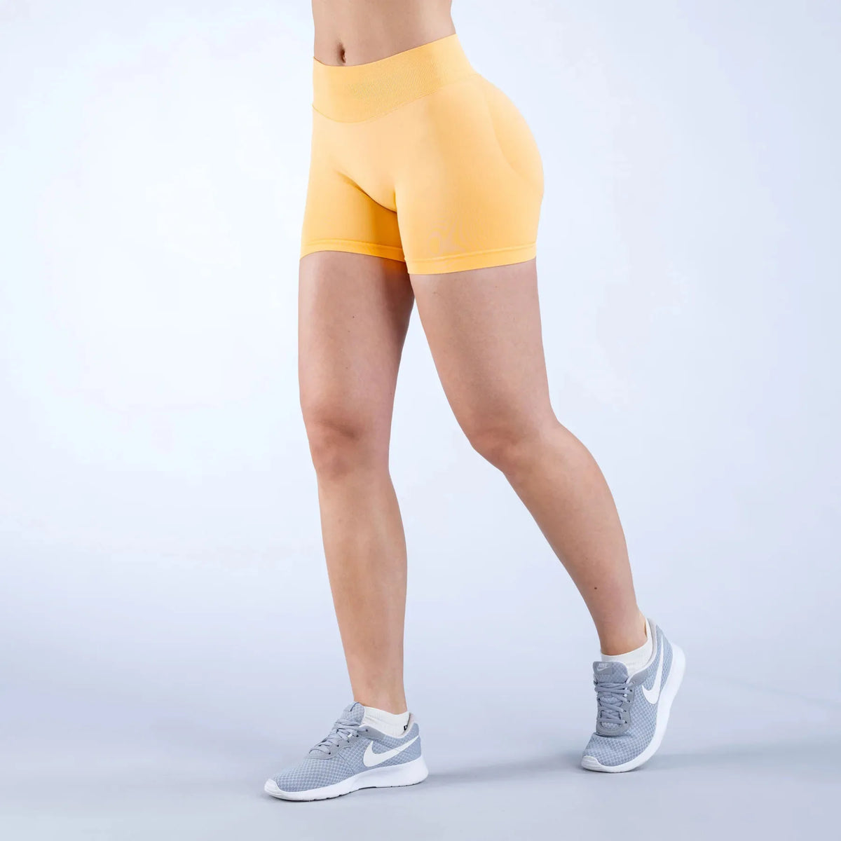 A person is modeling seamless high-waisted yoga shorts in a yellow color while standing.