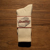 A pair of beige tube socks featuring a graphic that reads Quality on a stylized piece of fabric.