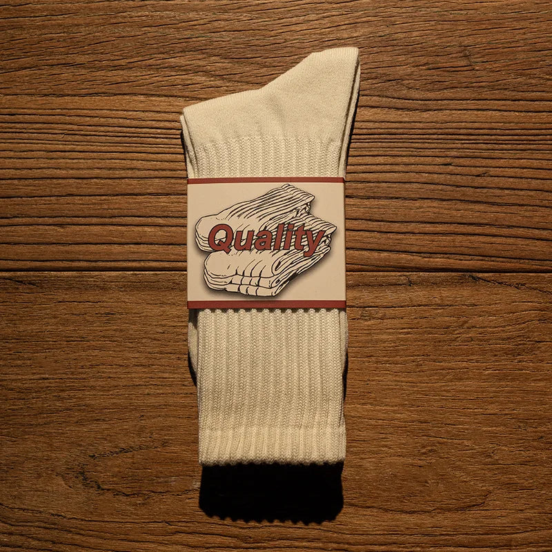 A pair of beige tube socks featuring a graphic that reads Quality on a stylized piece of fabric.