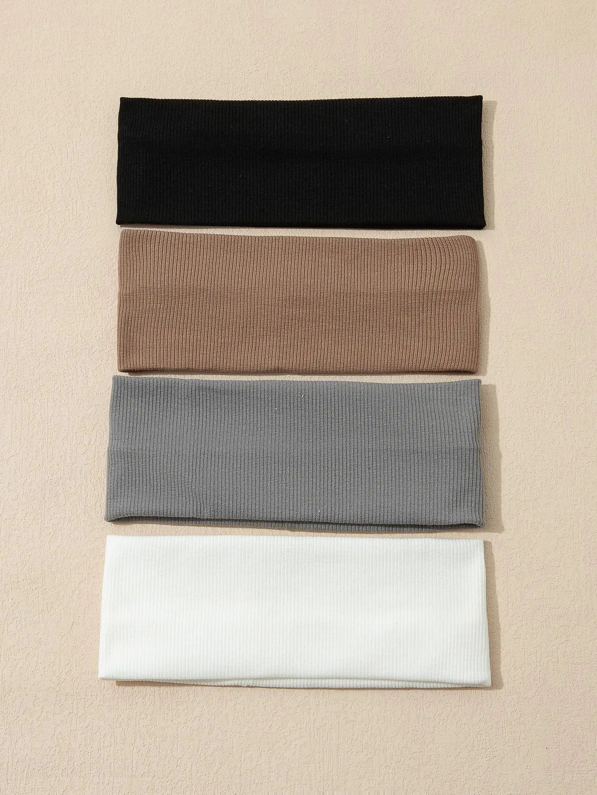 Una pila de cuatro bandas elásticas para el cabello en negro, marrón, gris y blanco.