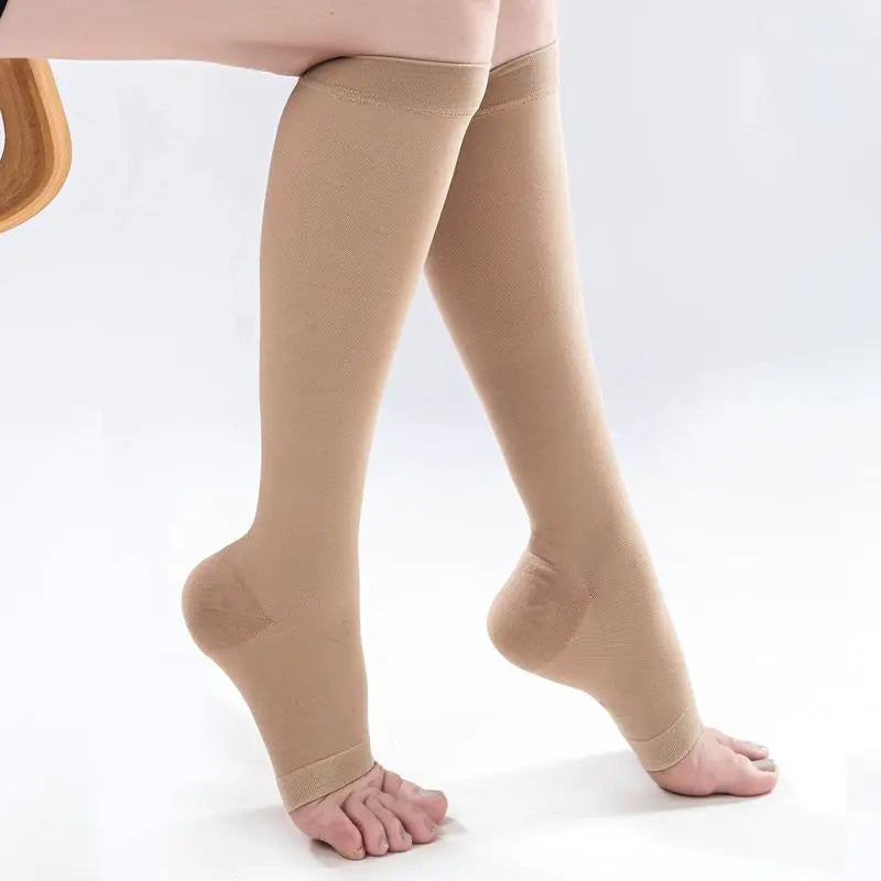 A pair of beige medical grade knee high compression stockings worn on a person's legs.