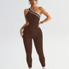 A model wearing a seamless, dark brown yoga jumpsuit with white trim and gold jewelry.