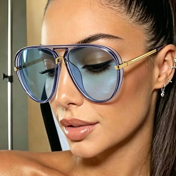 A close-up of a woman wearing classic oval pilot sunglasses with gold accents and blue-tinted lenses.