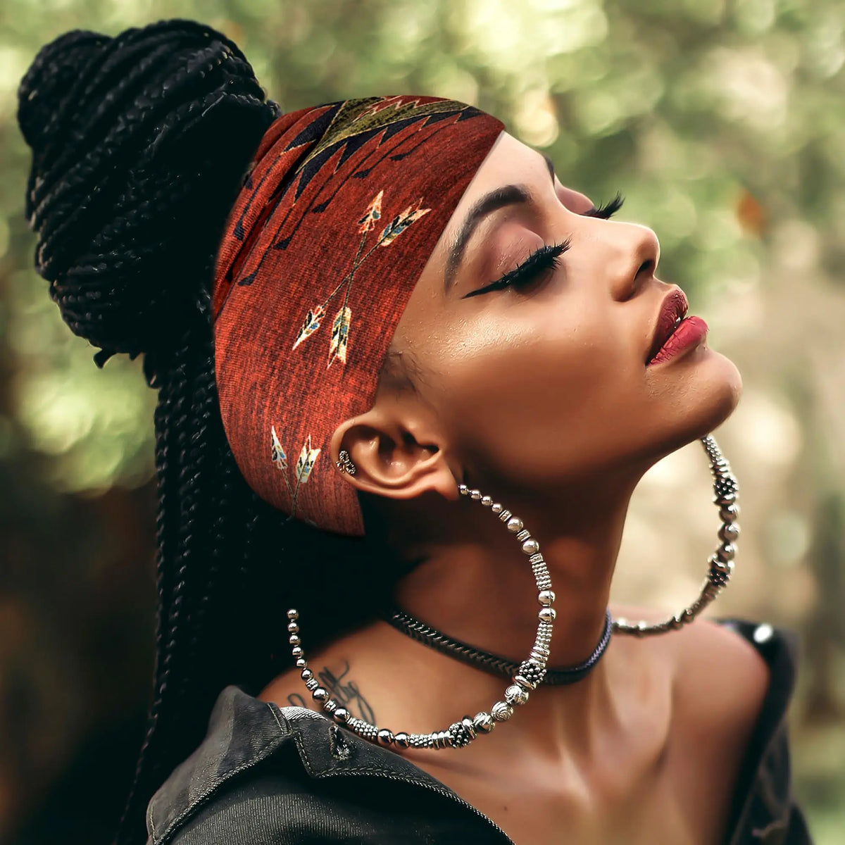 A woman with braided hair wears a terracotta-colored bandana headband outdoors.