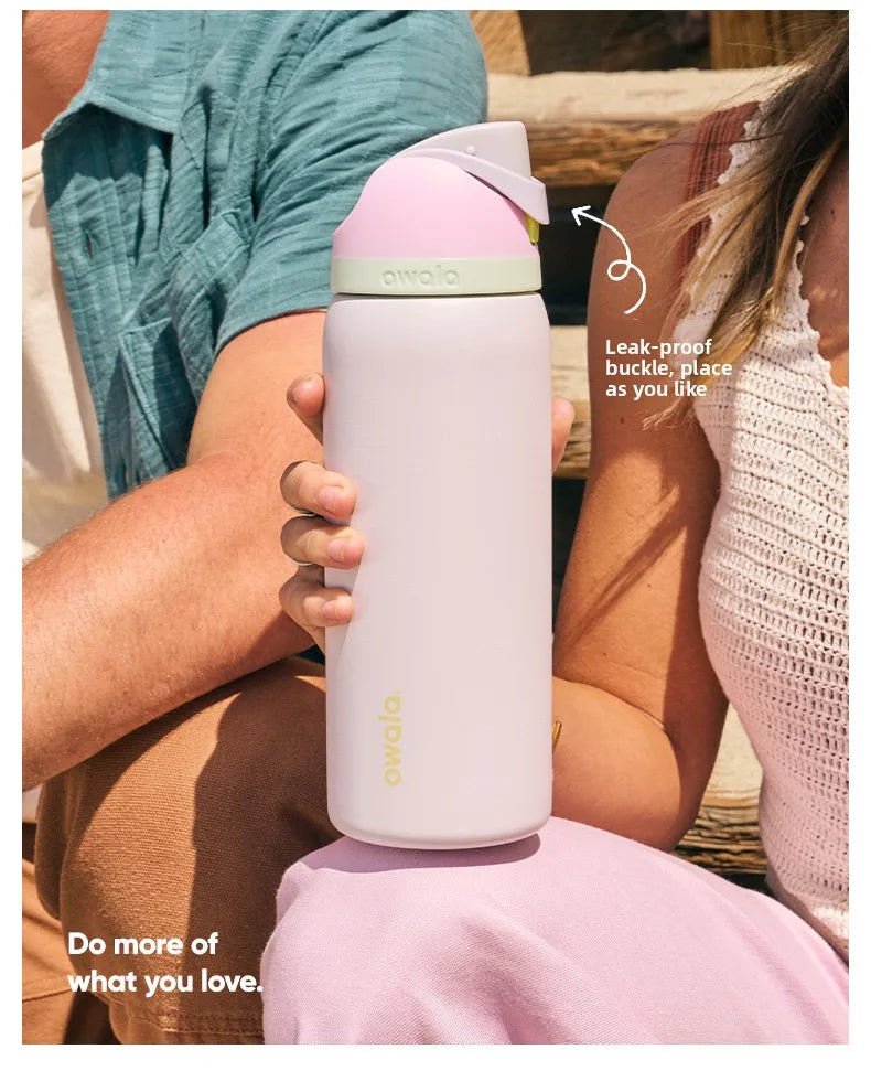 Eine Person hält eine rosa Owala isolierte Wasserflasche mit Strohhalm vor einer natürlichen Außenkulisse.