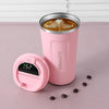 A pink insulated thermos bottle with a lid and a coffee drink inside, resting on a pink surface.