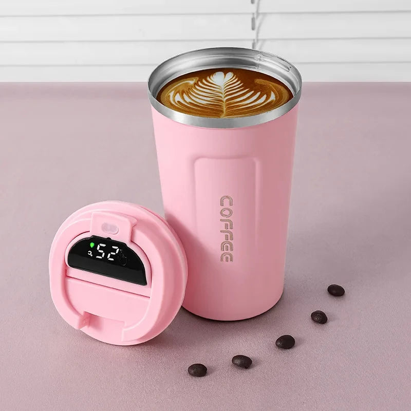A pink insulated thermos bottle with a lid and a coffee drink inside, resting on a pink surface.