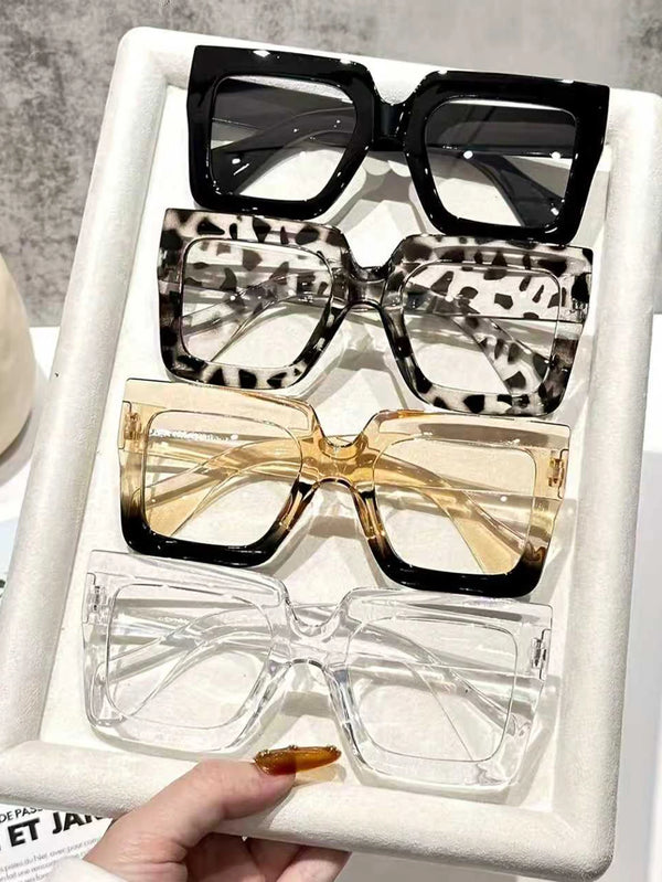 A display of four oversized rectangular reading glasses in black, leopard print, amber, and clear frames.
