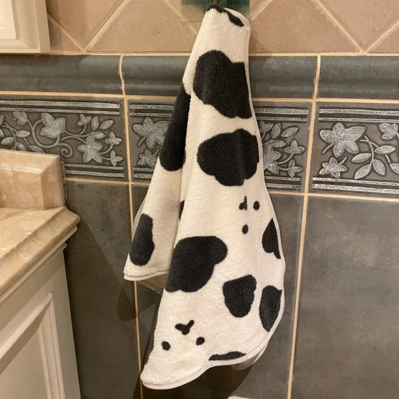 A white and black cow print face towel hanging on a tiled wall.