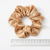 A beige satin scrunchie tied in a bow shape, measured against a ruler.