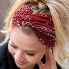 A close-up of a blonde woman wearing a red patterned boho headband in her hair.
