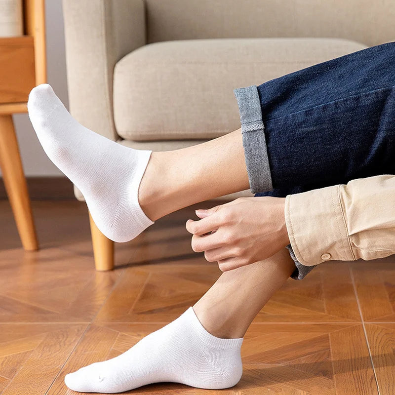 A close-up of a man's foot wearing white breathable ankle socks while standing on a wooden floor.